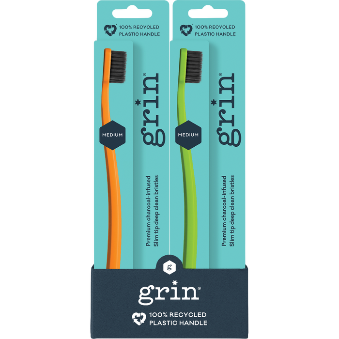 Two GRIN toothbrushes in packaging with teal and navy design.
